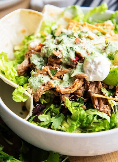 A close up of a copy cat of costa vida sweet pork salad with tomatillo ranch on top of a pile of pork with other taco toppings.