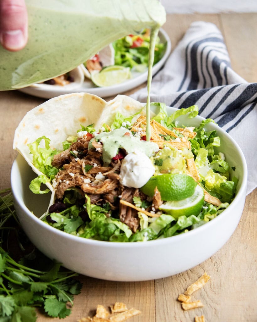 A hand pouring a green tomatillo cilantro ranch on a taco salad dressing.