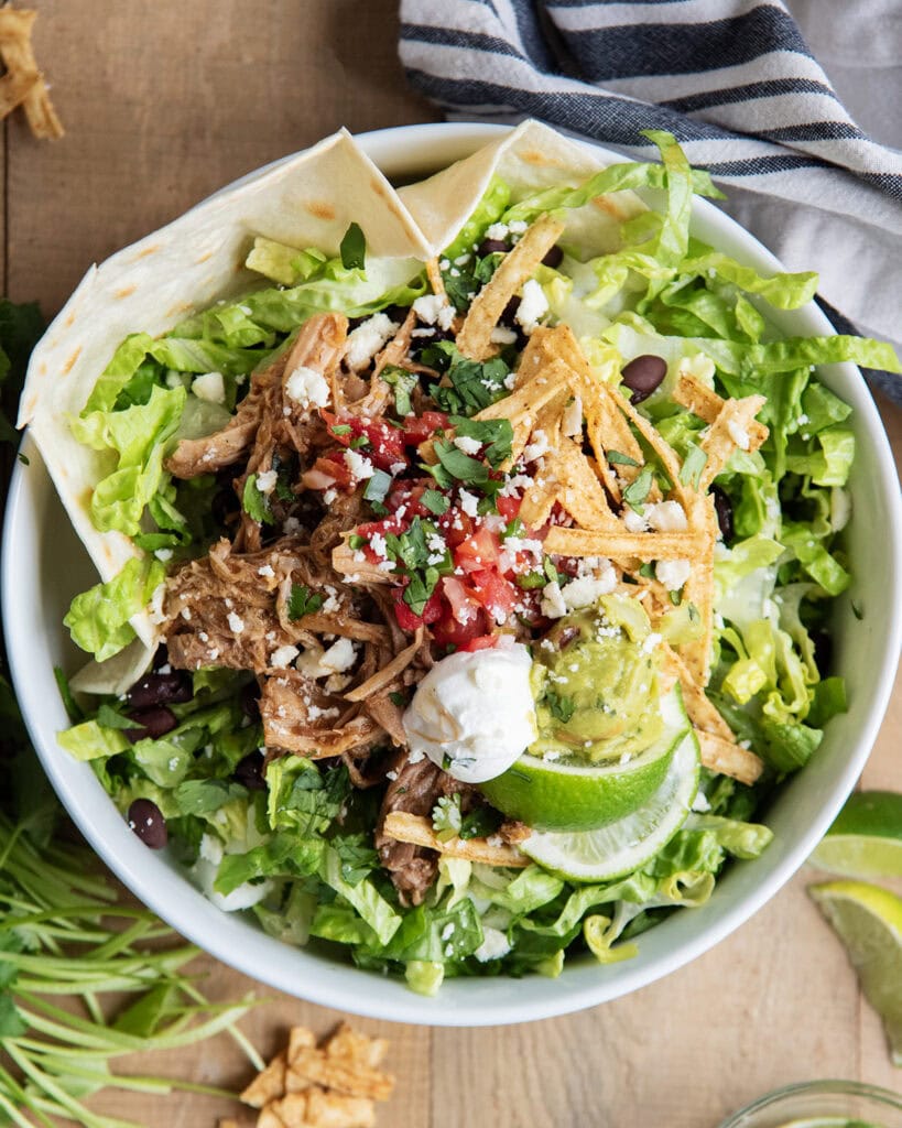An above view of a copycat cafe rio pulled pork salad, with sweet pork, tortilla strips, sour cream, guacamole, and pico on lettuce.