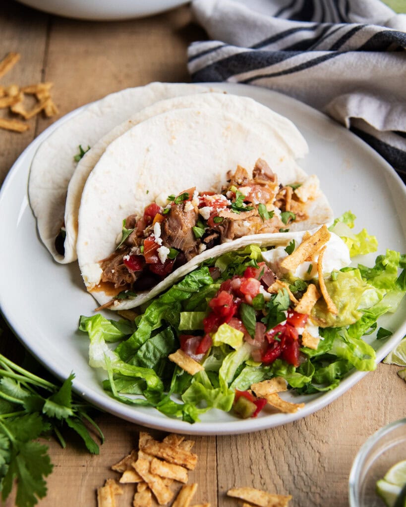 A plate of two pork tacos next to a pile of lettuce and pico de gallo.