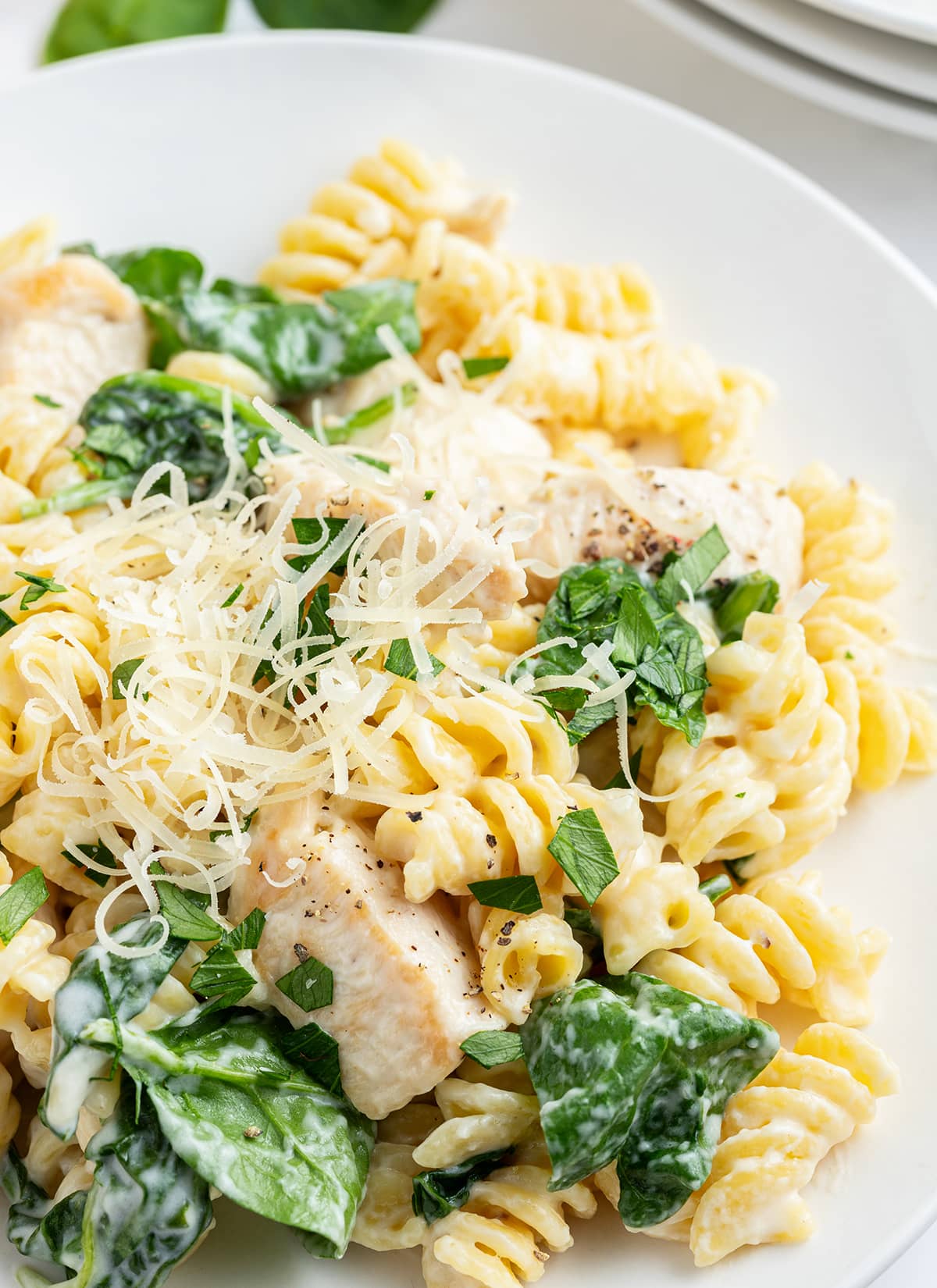 A plateful of creamy lemon chicken pasta with spinach, topped with freshly grated parmesan cheese.