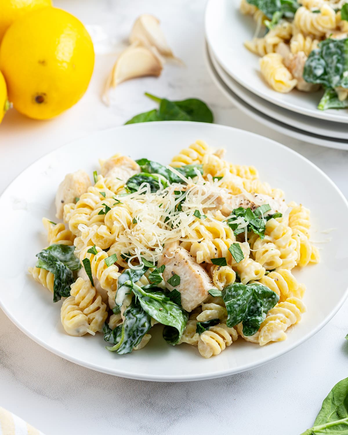 A plateful of pasta covered in a lemon cream sauce, with chicken pieces and spinach, and parmesan on top.