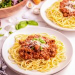 A plate of spaghetti topped with a meat sauce and fresh basil.