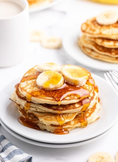 A stack of banana pancakes on a plate topped with banana slices and syrup.