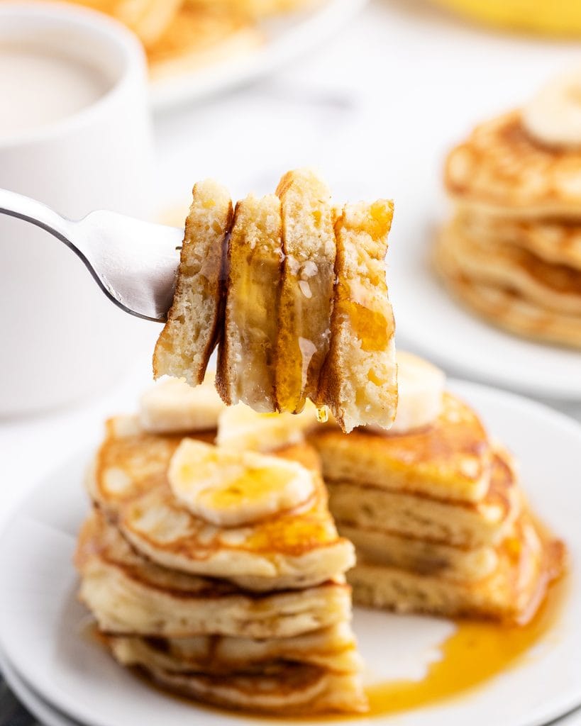 Four pieces of pancakes on a fork being held above a plate of pancakes.