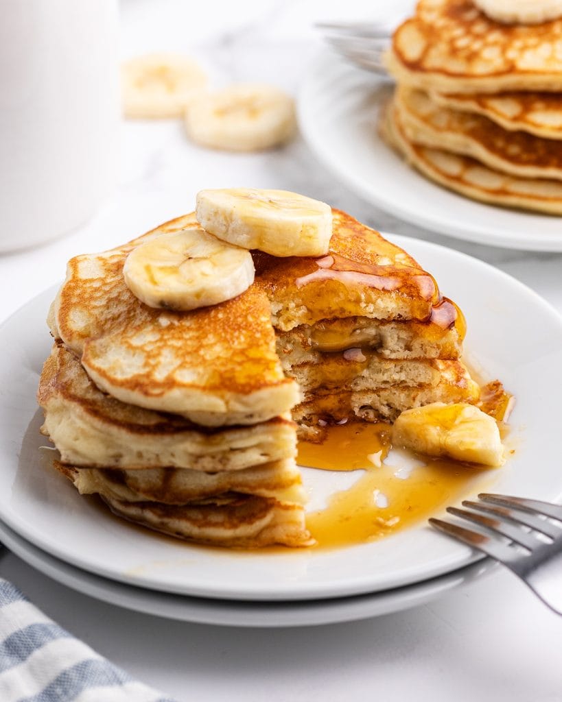A stack of four pancakes on a plate toppe dwith bananas, and a quarter of the pancakes are cut out and removed.