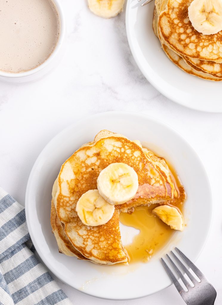 An overhead photo of banana pancakes on a plate topped with syrup and banana slices.