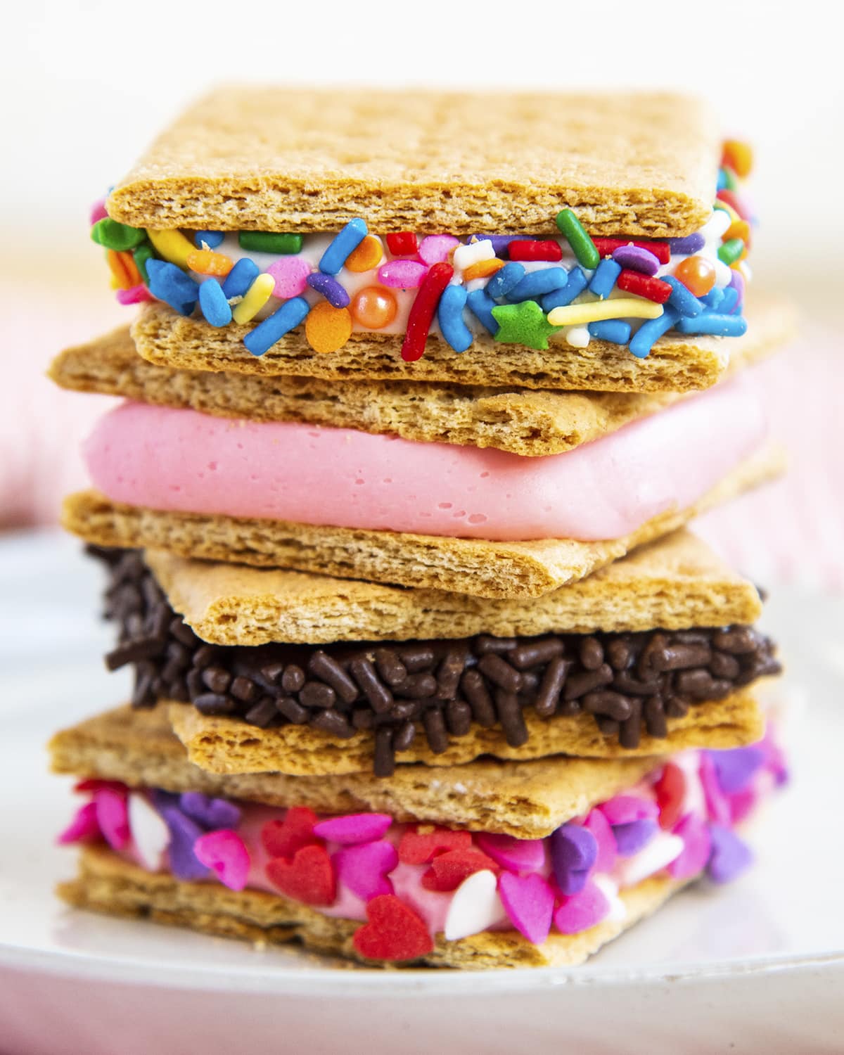 A stack of graham crackers full of frosting in the middle. There are 4 in the stack, with sprinkles on the outsides of three of them.