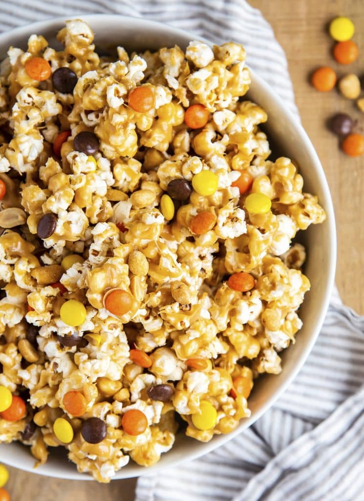 An overhead shot showing part of a bowl of peanut butter popcorn, full of reeses pieces candies, and peanuts.