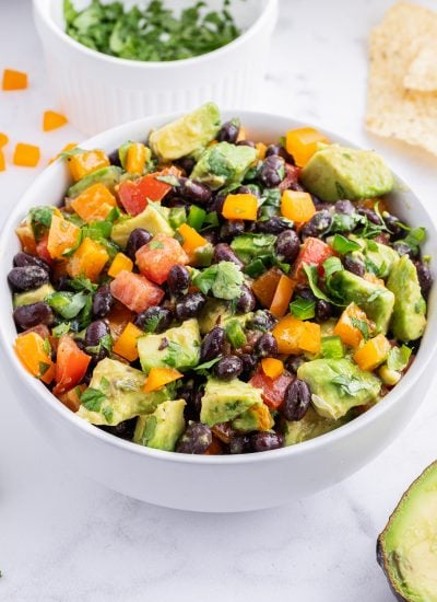 A close up of a bowl of avocado black bean salad with tomatoes and bell peppers.