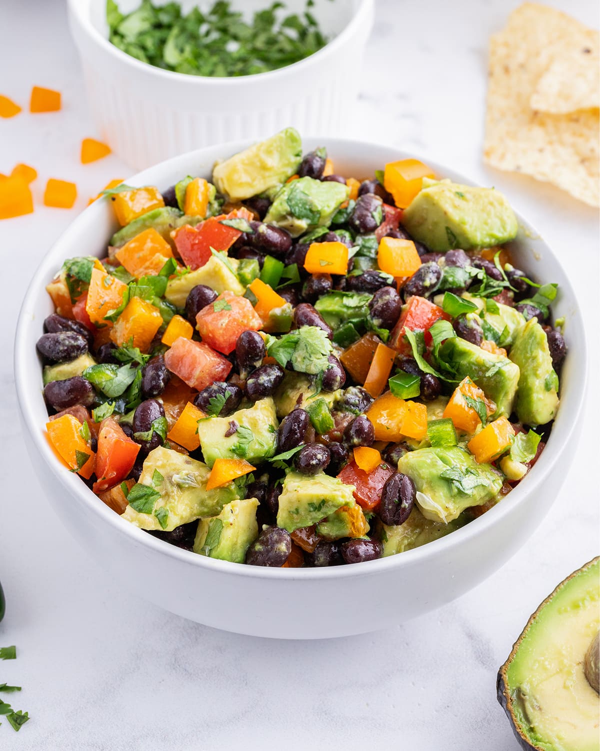 A close up of a bowl of avocado black bean salad with tomatoes and bell peppers.