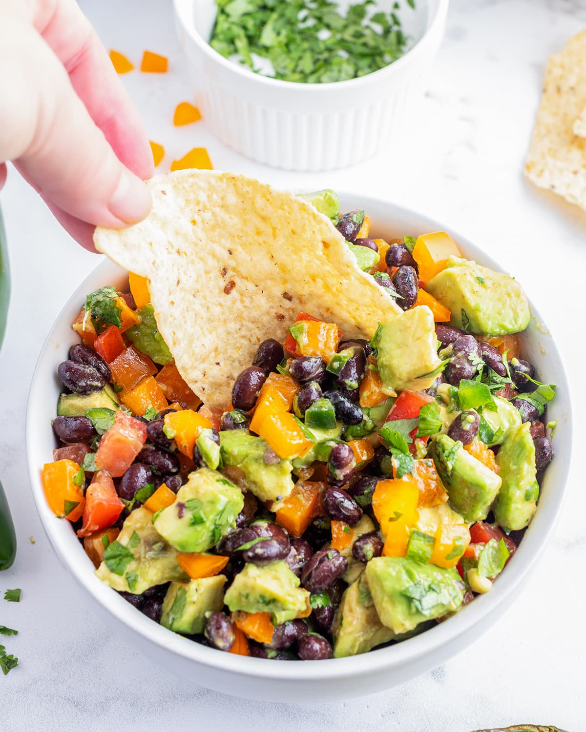 An overhead photo of avocado and black bean salad with a tortilla chip dipping into it.