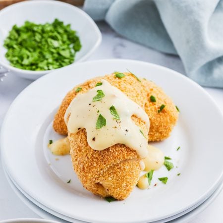 A plate of two breaded chicken crescent roll ups topped with gravy and fresh parsley.
