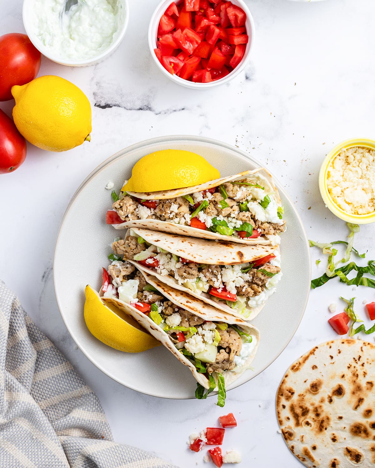 An overhead photo of three greek tacos on a plate with lemon wedges on the side of them. 