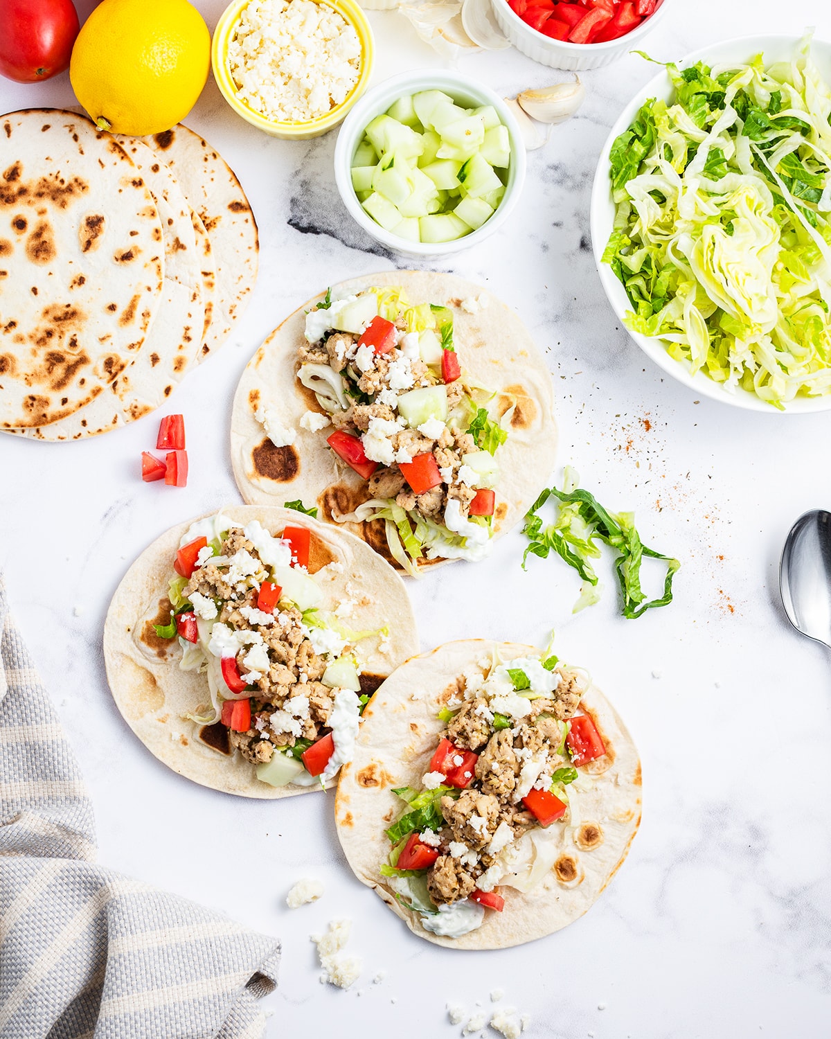 An overhead photo of tortillas topped with ground chicken, feta, and diced tomatoes.