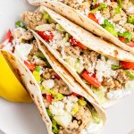 A close up of Greek chicken tacos topped with lettuce, feta, and tomatoes.