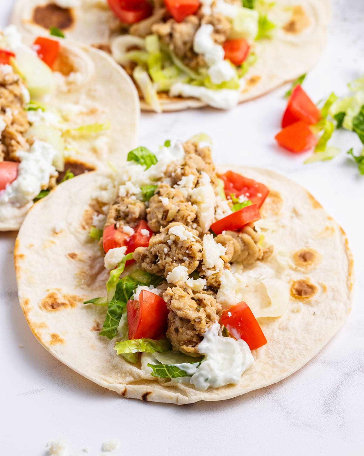 A greek chicken taco in a tortilla topped with tomatoes and lettuce.