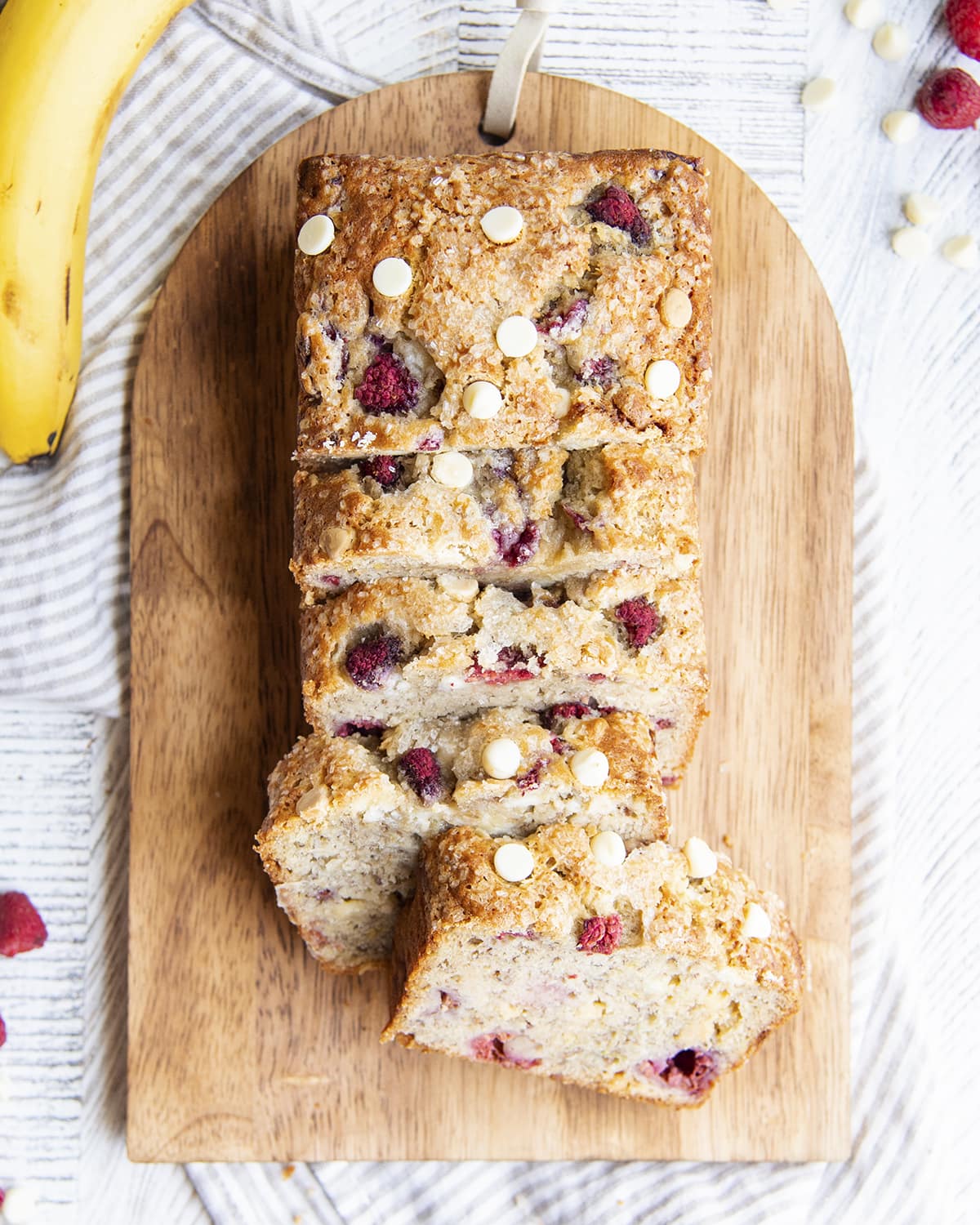 Cut up slices of banana bread with white chocolate and raspberries on a cutting board.