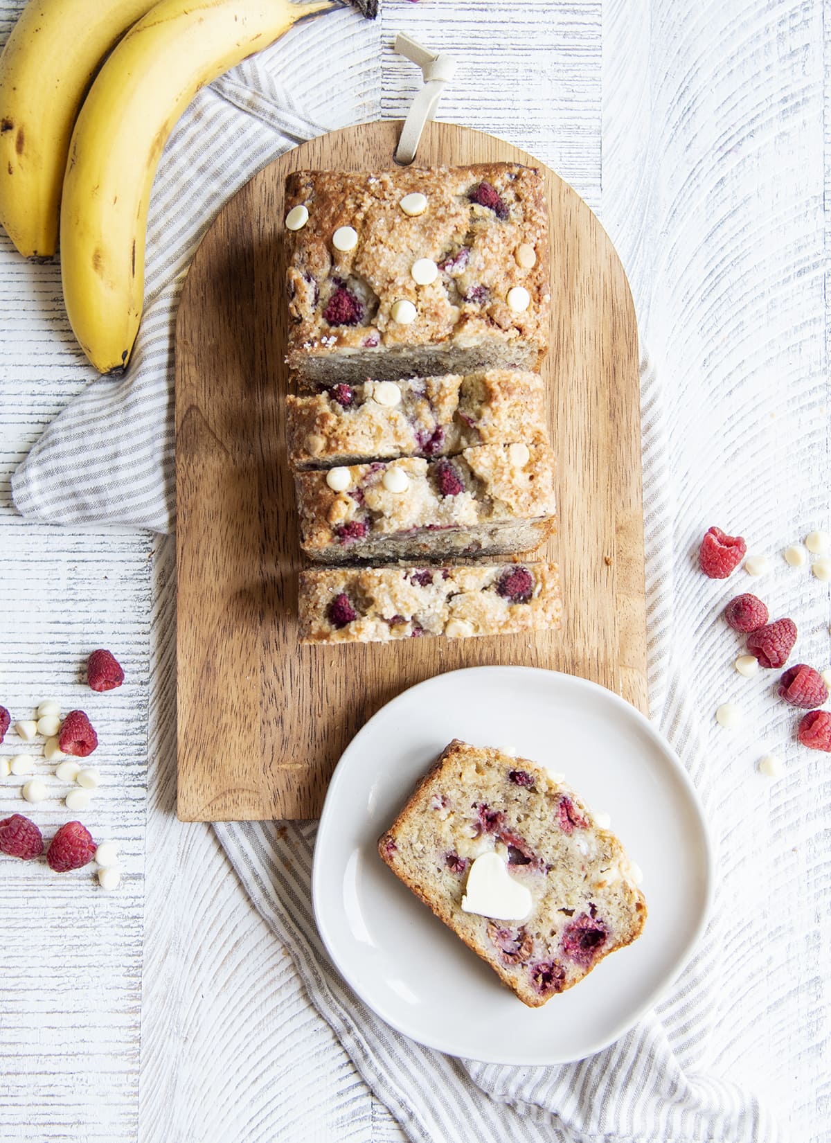 A slice of raspberry white chocolate banana bread on a plate, next to the loaf of it.
