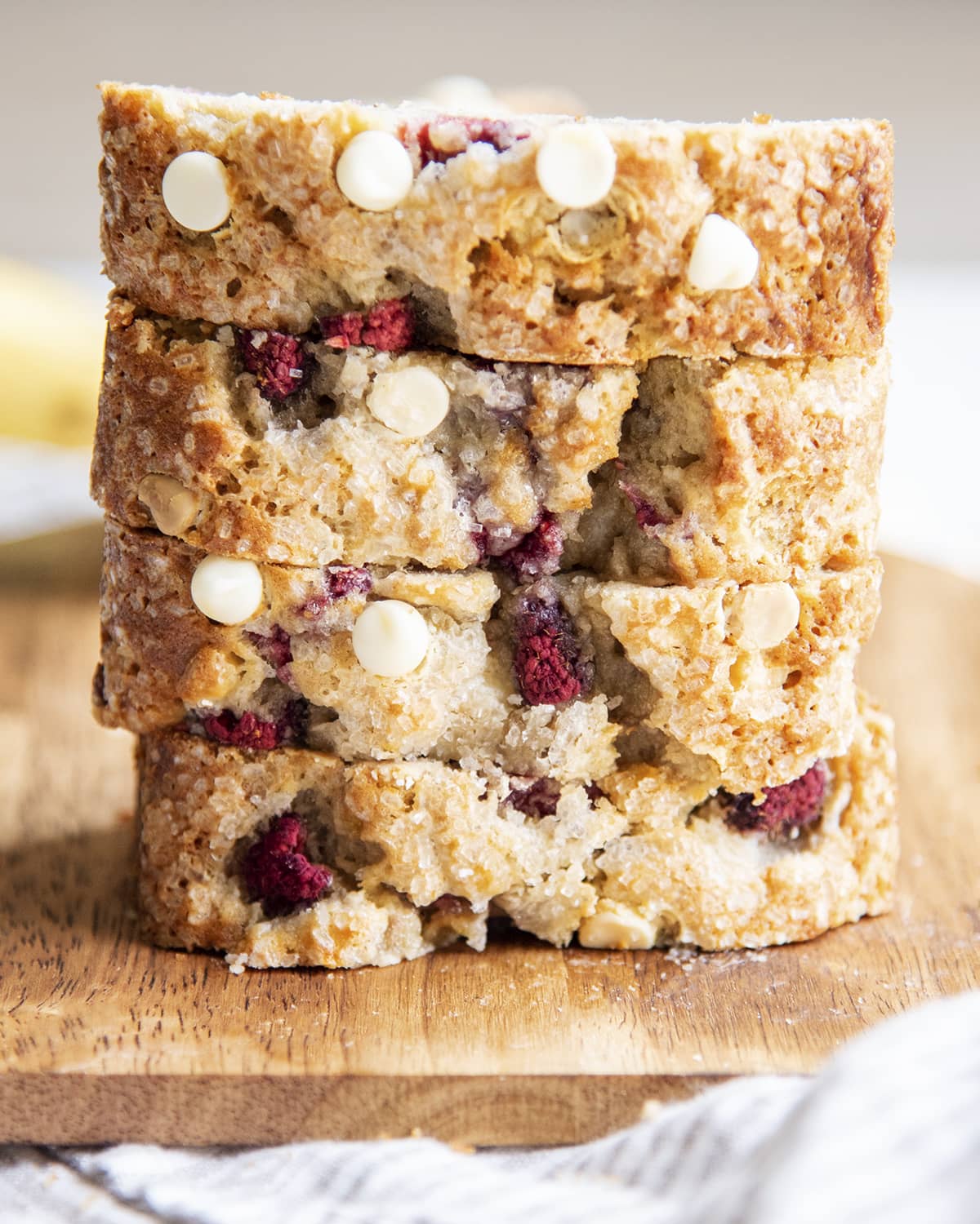 A stack of four thick slices of raspberry white chocolate banana bread on a cutting board.