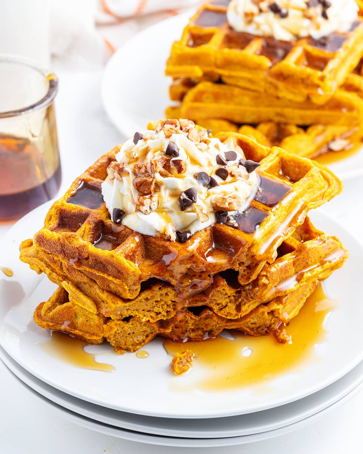 A stack of 3 pumpkin waffles on a plate, with a fork bite out of each.