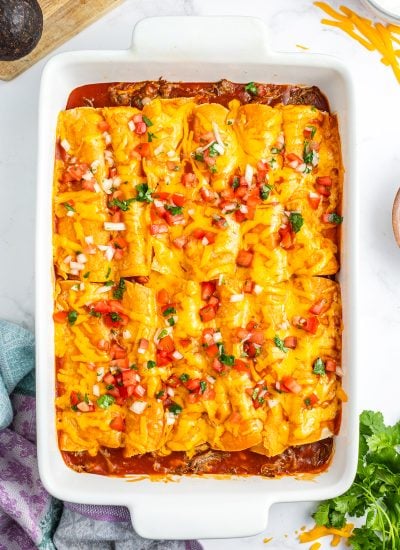 A pan of cheese covered enchiladas topped with pico de gallo.