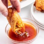 A hand dipping a cut chicken egg roll into sweet and sour sauce.