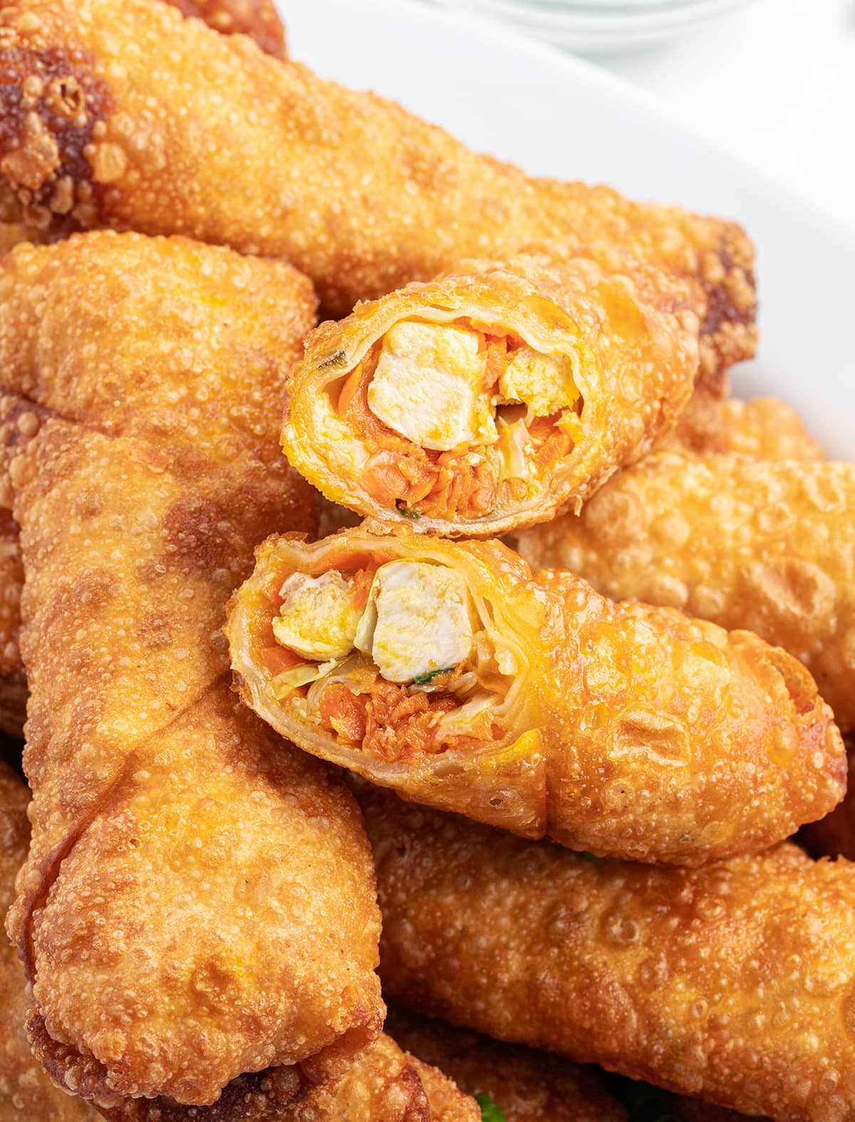 A pile of chicken egg rolls, with one cut open showing the chicken and vegetables in the middle. 