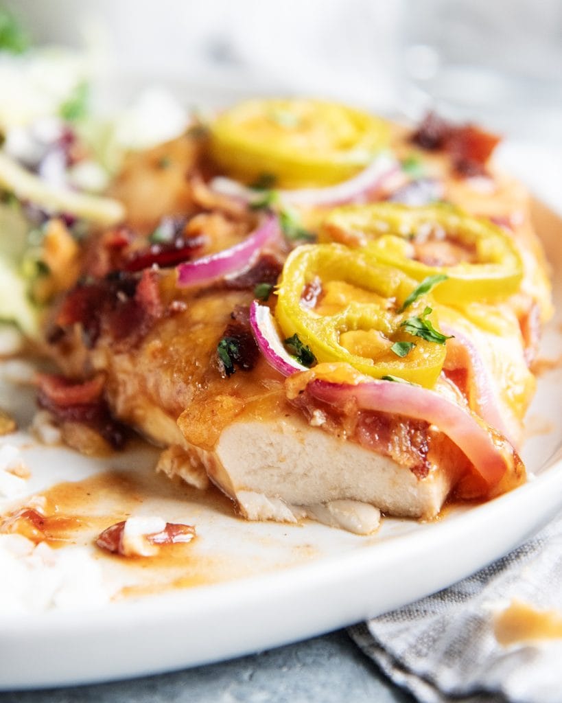 A chicken breast topped with cheese, red onion, and jalapenos, with a bite cut out.