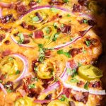 A baking pan of BBQ baked chicken breast topped with cheese, red onion, and jalapenos.