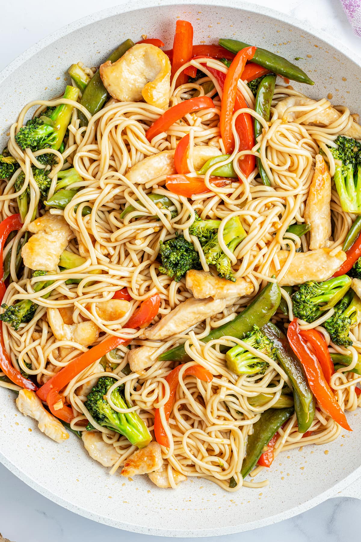 A skillet pan full of a homemade chicken lo mein with broccoli and red bell pepper.