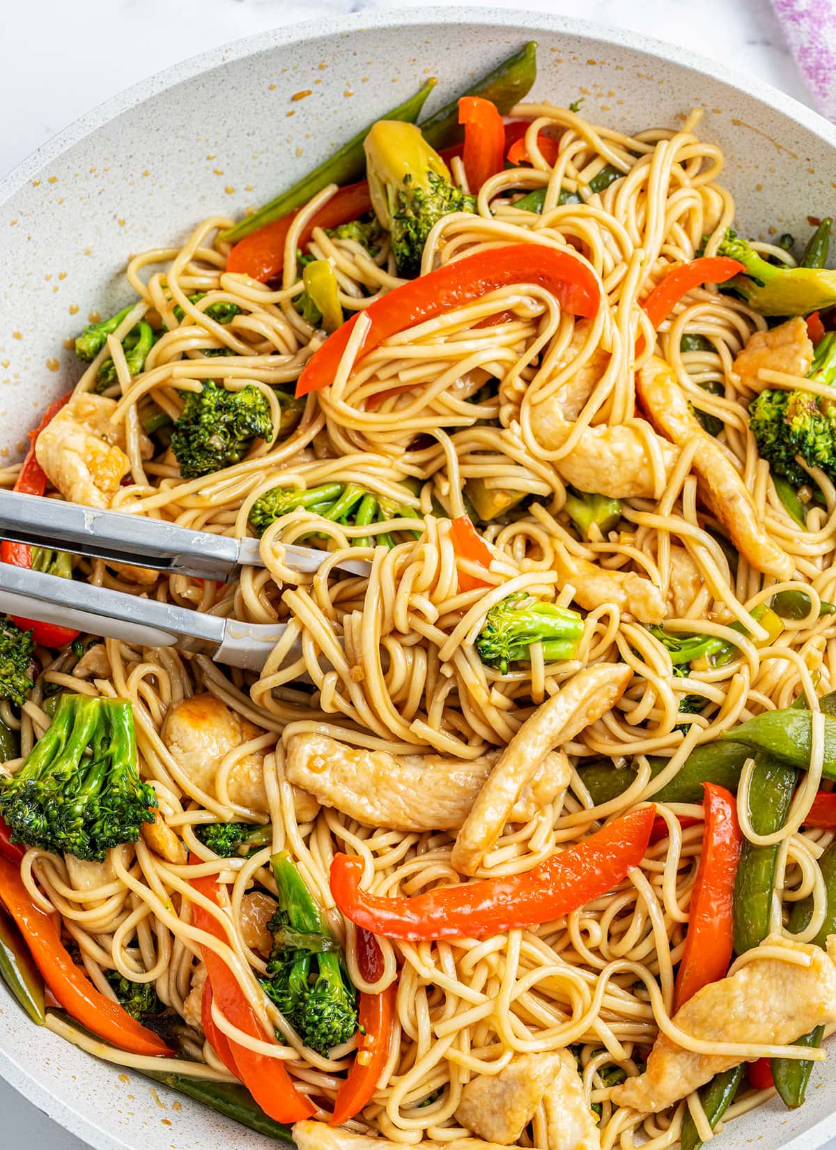 A skillet pan full of a homemade chicken lo mein with broccoli and red bell pepper.