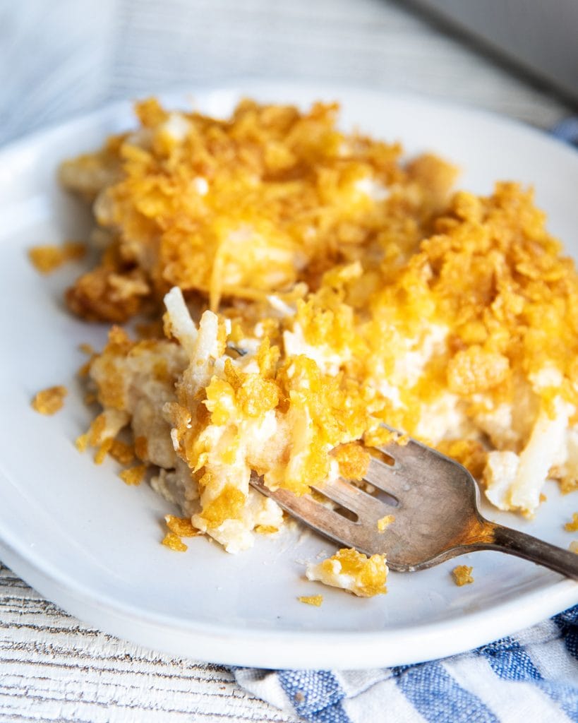 A plate of hashbrown potato casserole, with a bite of it on a fork.