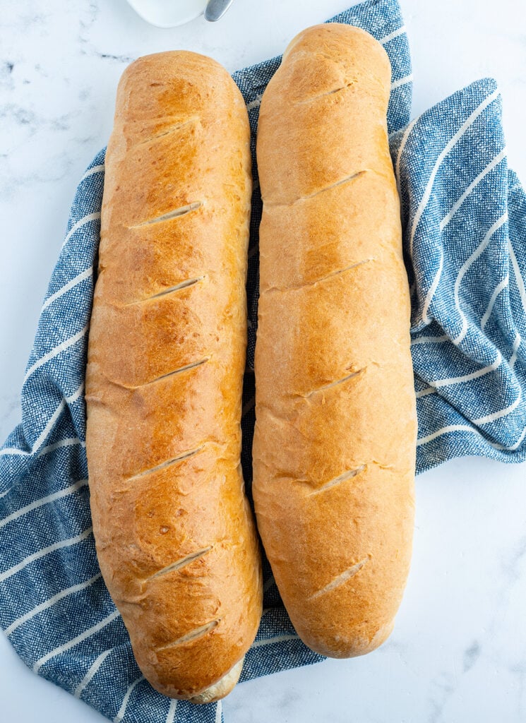 Two loaves of golden French bread on a blue towel.