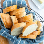 A basket lined with a blue towel, with slices of French bread.