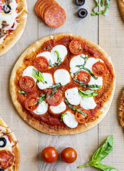 An overhead photo of a pita pizza topped with mozzarella dollops, tomatoes, and fresh basil.