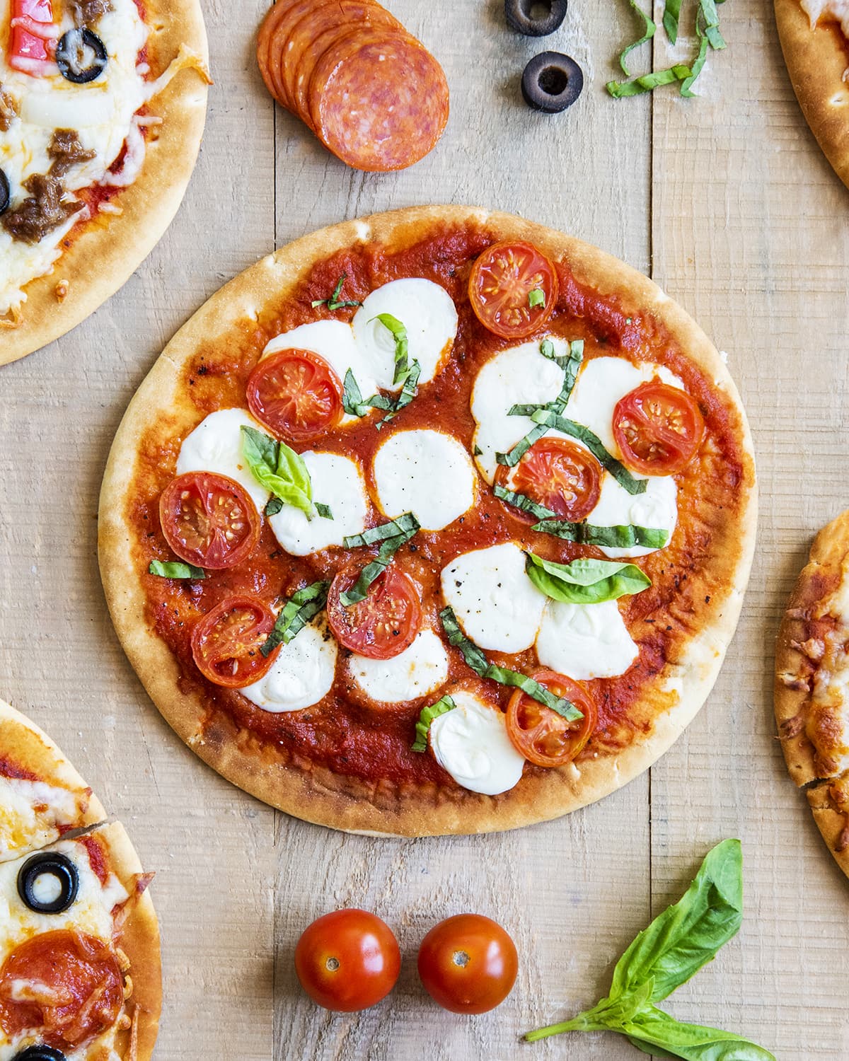 An overhead photo of a pita pizza topped with mozzarella dollops, tomatoes, and fresh basil.