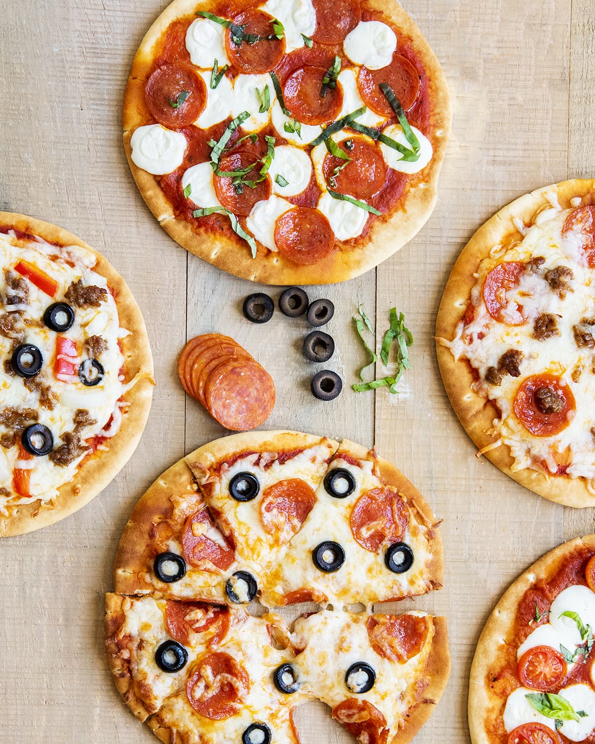 An overhead photo of pita pizzas with different toppings on each.