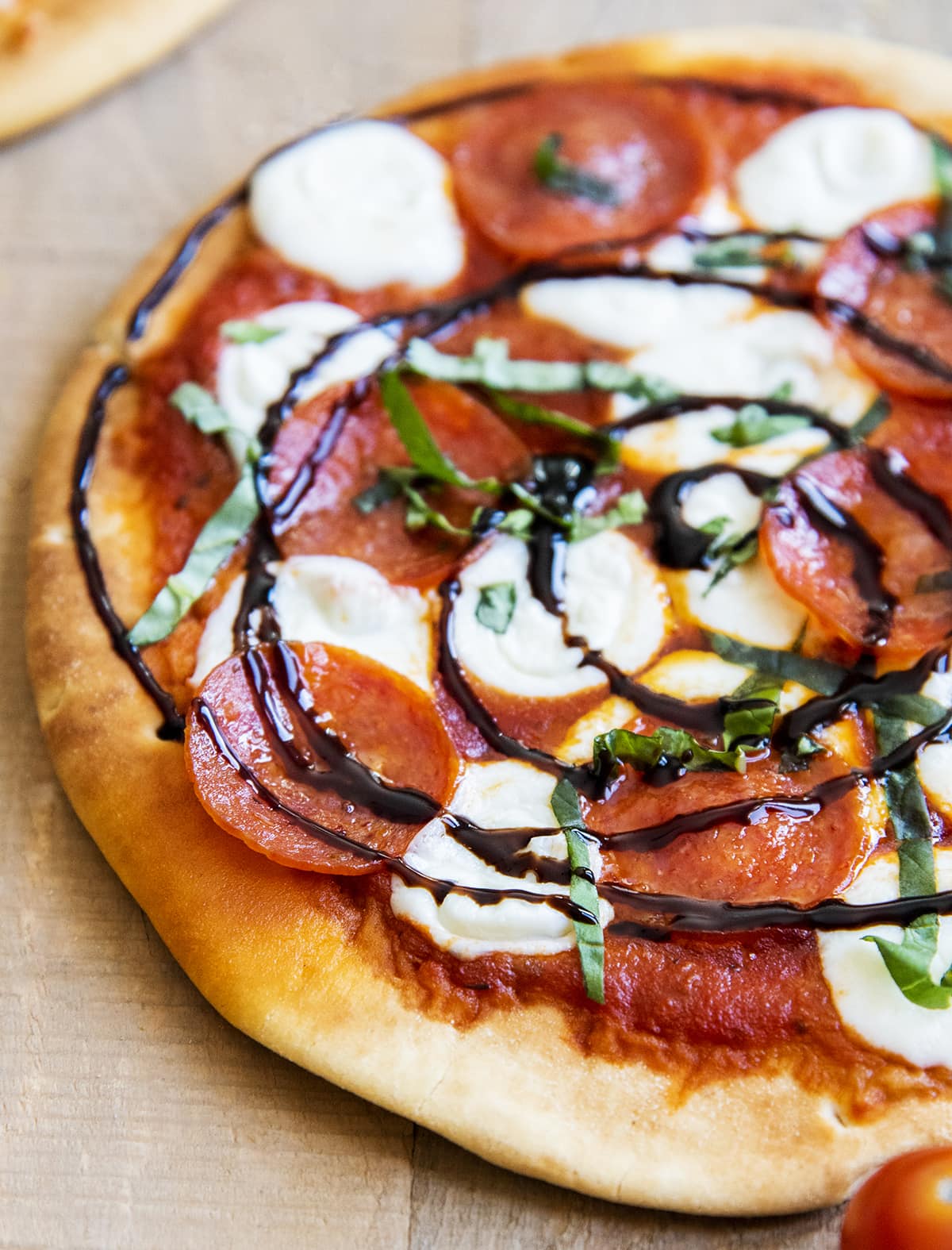A pepperoni and cheese pita pizza topped with fresh basil and balsamic vinegar glaze.