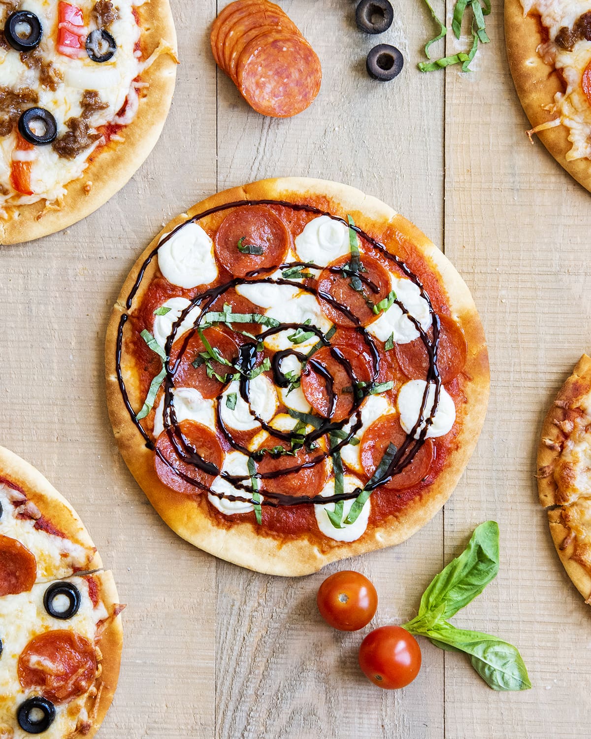 An overhead photo of a pepperoni and cheese pita pizza topped with fresh basil and balsamic vinegar glaze. 