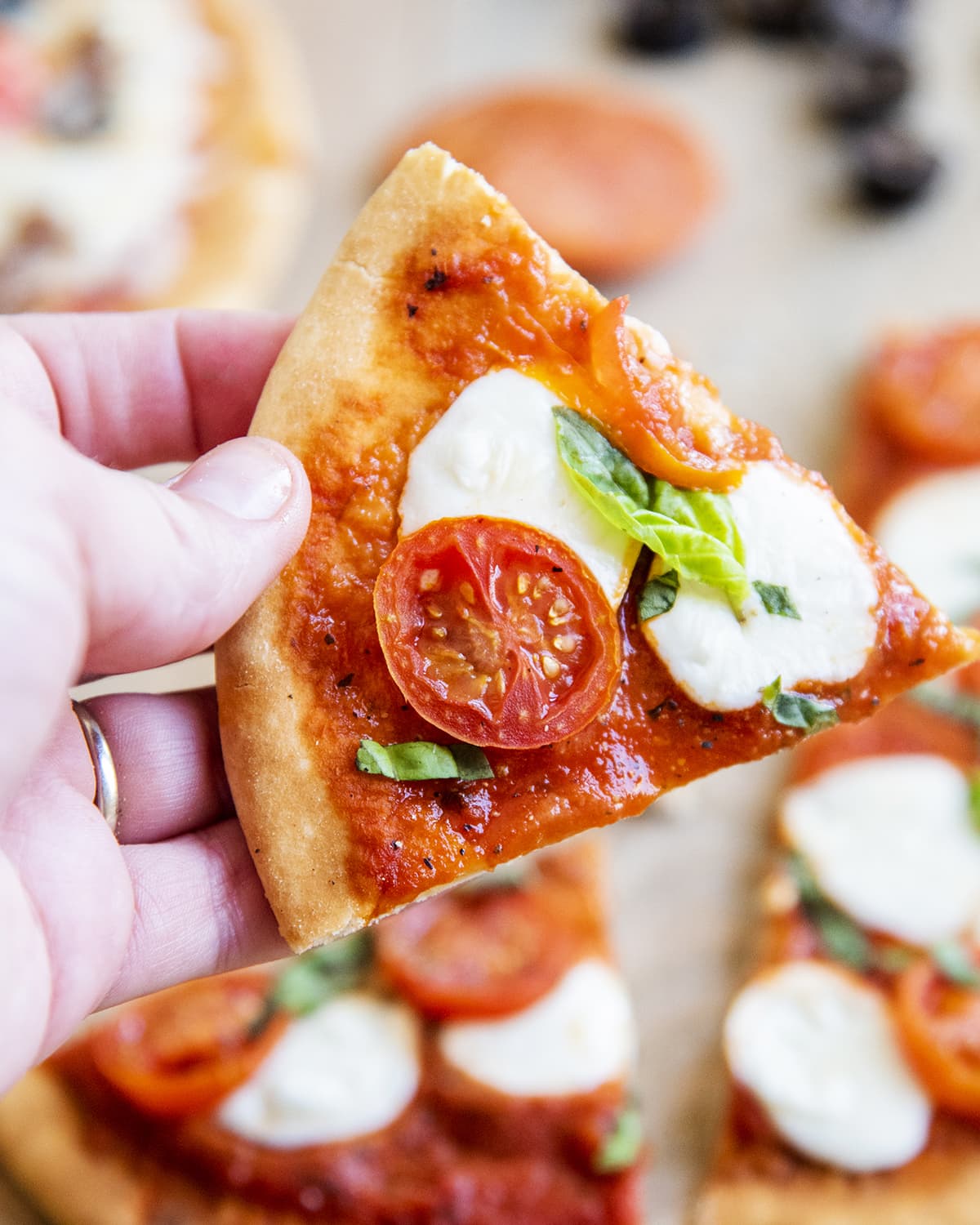 A hand holding a piece of pizza topped with mozzarella cheese, and a tomato slice.