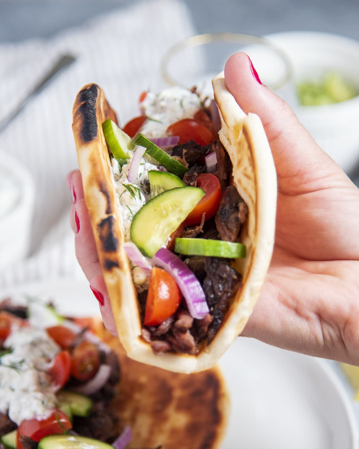 A hand holding a beef gyro wrapped in a pita. 