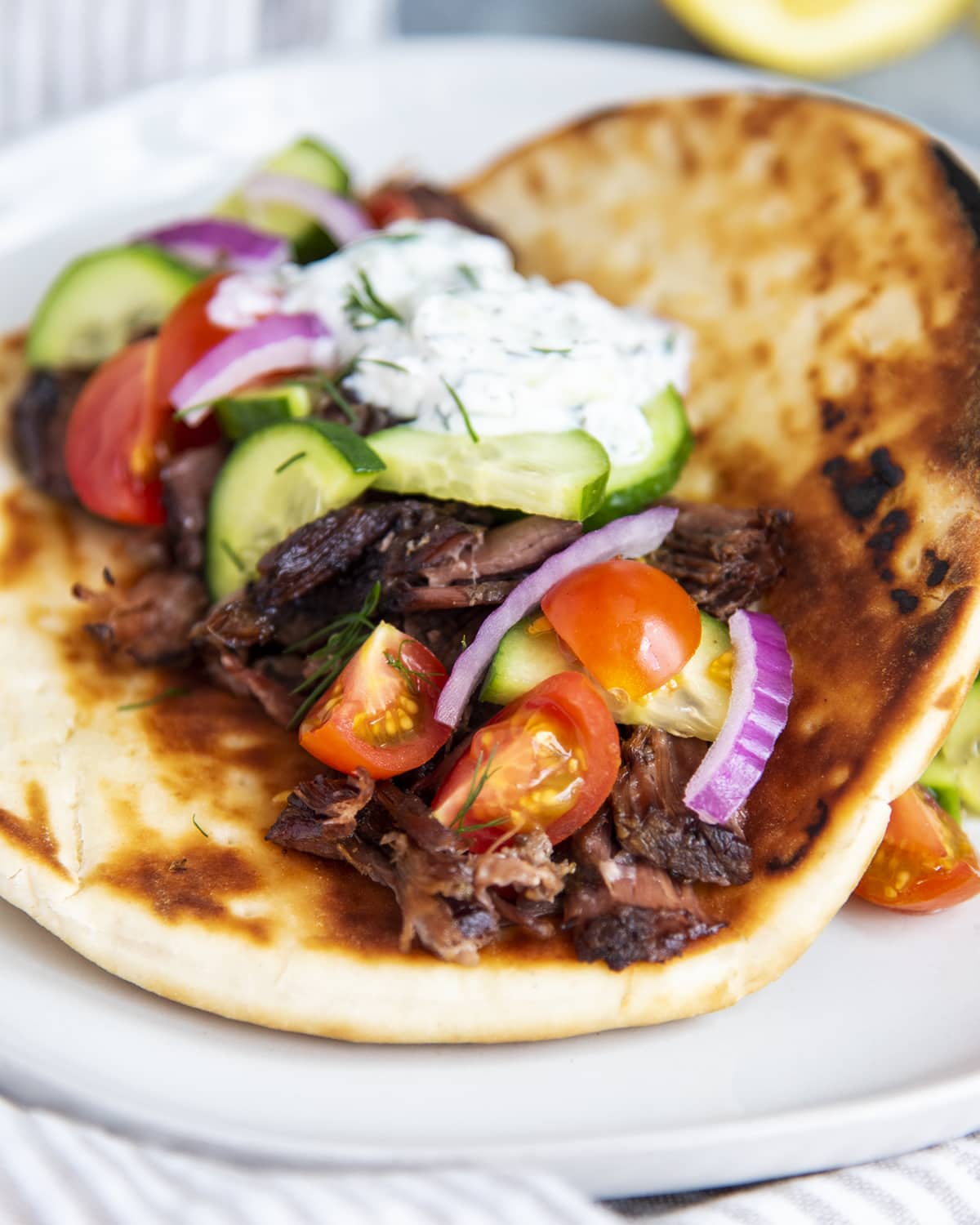 A beef gyro in a pita topped with tomatoes, onions, cucumbers, and tzatziki.