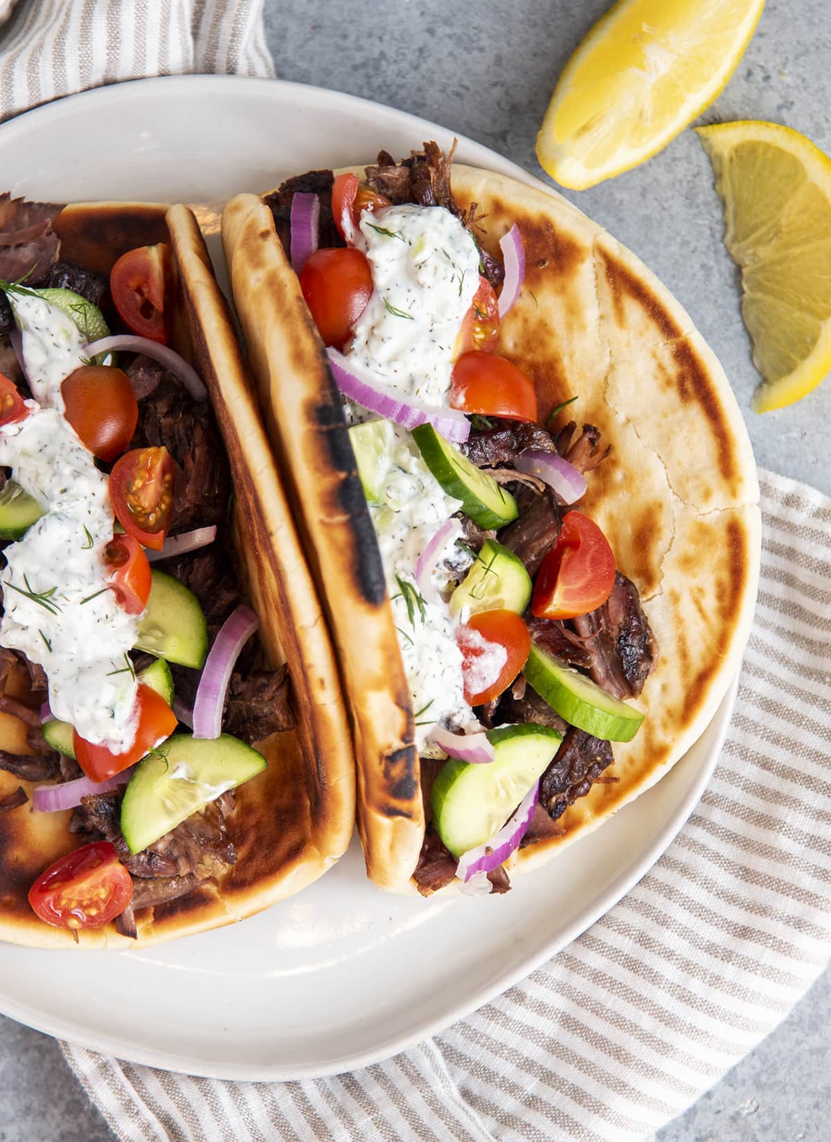 Two pitas topped with slow cooker beef gyro meat, and gyro toppings on a plate.