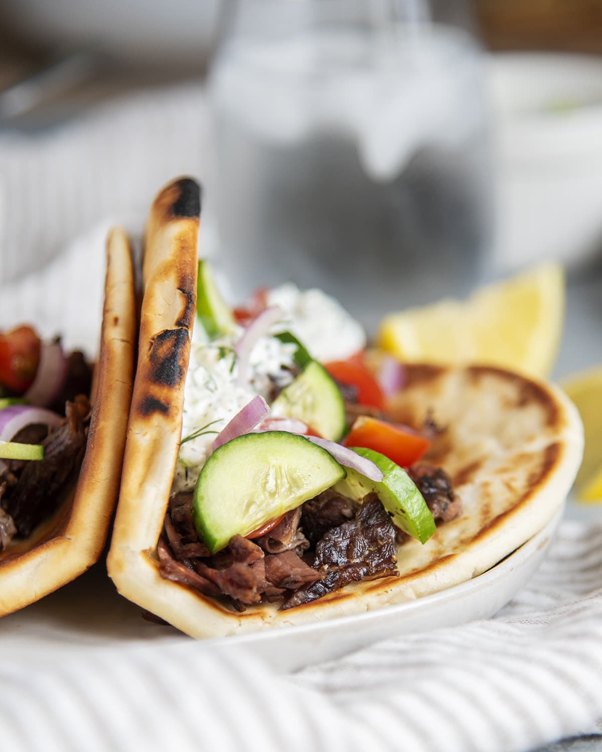 A plate of beef gyros in pitas with fresh vegetables and tzatziki on top.