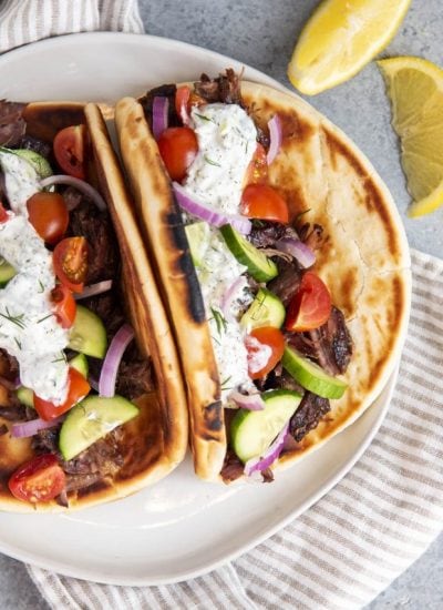 Two pitas topped with slow cooker beef gyro meat, and gyro toppings on a plate.