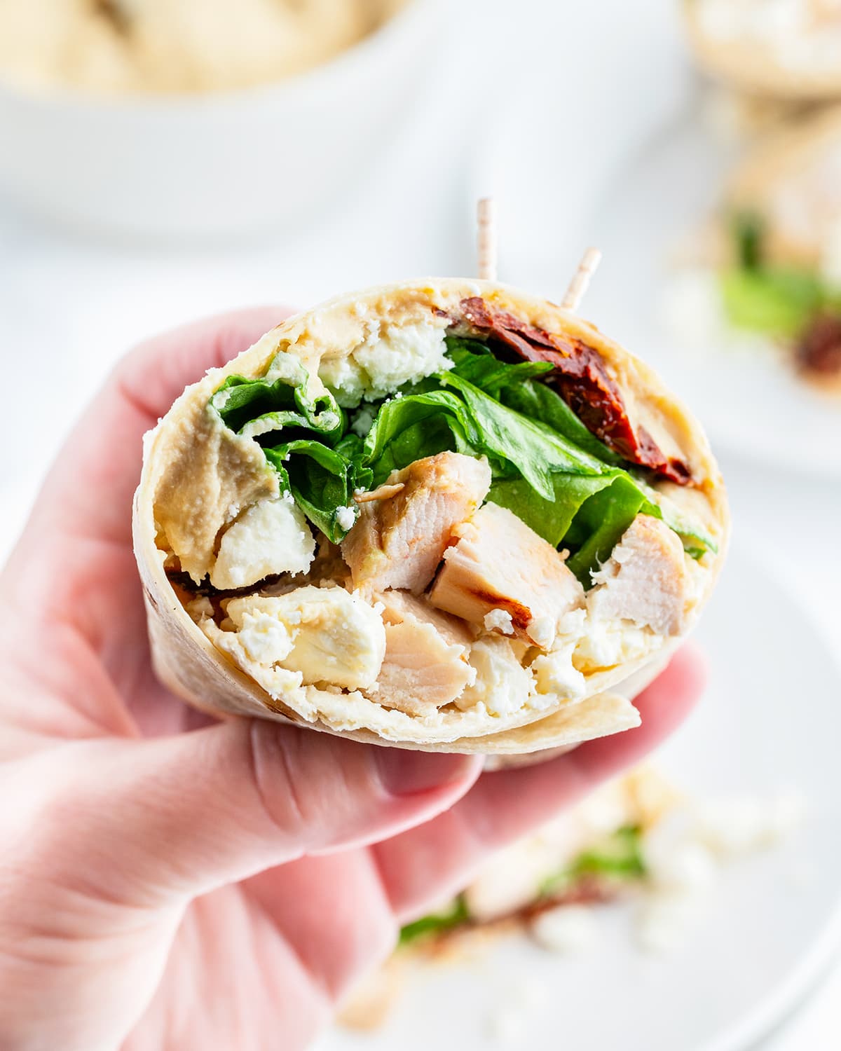 A hand holding half of a chicken wrap, full of lettuce, chicken, sundried tomatoes, and feta.