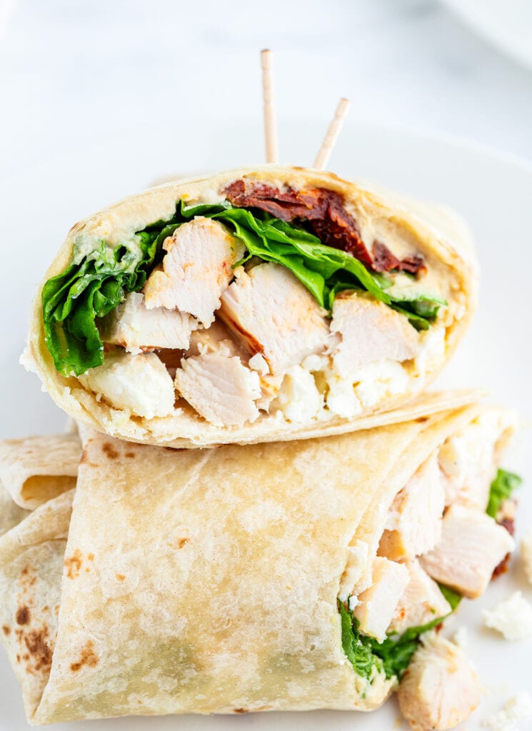 Half of a chicken wrap with pieces of chicken, lettuce, sundried tomatoes, and feta.