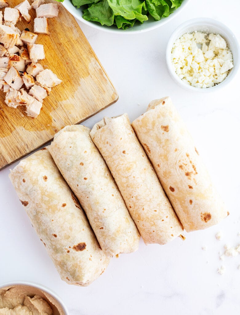 Four chicken wraps rolled up on a white counter top.