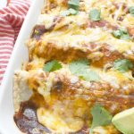 A close up of red sauce chicken enchiladas with cheese melting and cilantro sprinkled on top in a white baking pan